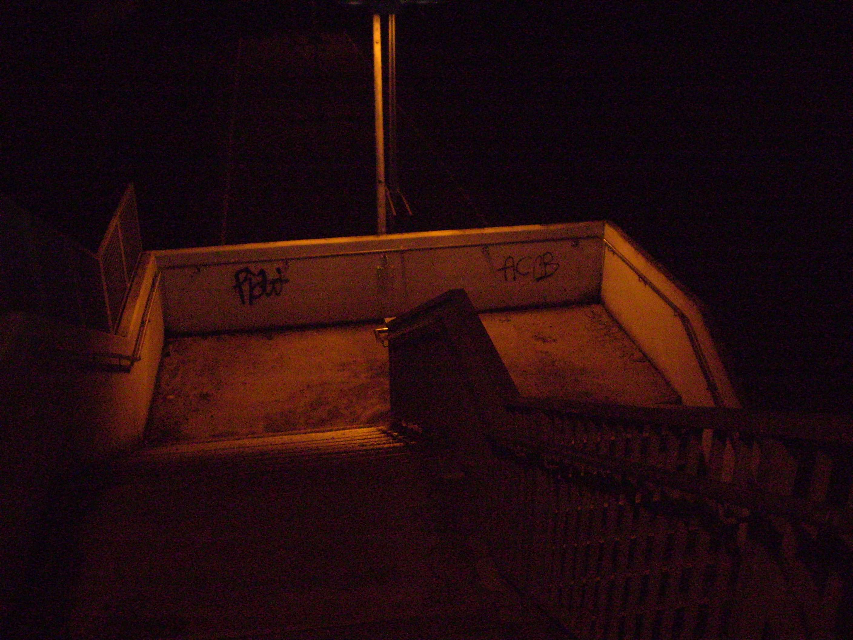 staircase with a curve going downwards. On it's walls graffity reads, 'ACAP' and with a Tag. Night shourds the dimly orange hue that envelops the walkable parts of the staircase. It's left to imagination what could be behind the stairs.